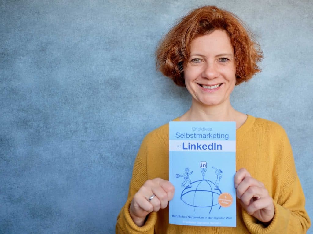 LinkedIn Expertin Friederike Gonzalez Schmitz hat die 4. Auflage ihres LinkedIn-Buches "Effektives Selbstmarketing mit LinkedIn" in der Hand und lächelt in die Kamera.